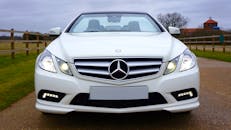 一辆白色梅赛德斯-奔驰敞篷车行驶在乡村道路上，尽显奢华与优雅