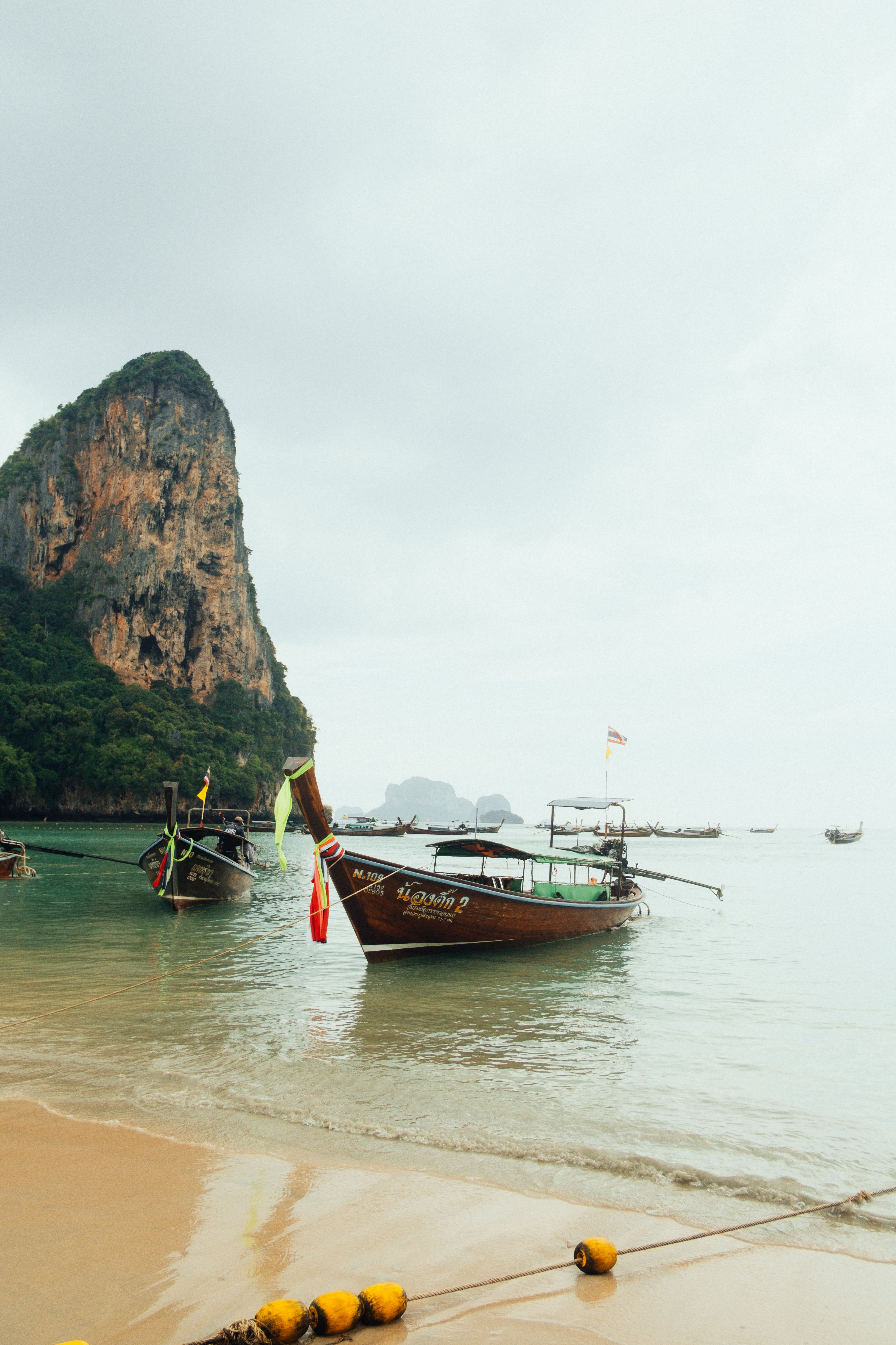 Longtail boats anchored off a limestone cliff beach in Krabi, Thailand