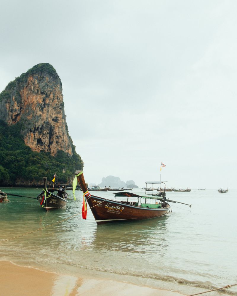 Longtail boats anchored off a limestone cliff beach in Krabi, Thailand