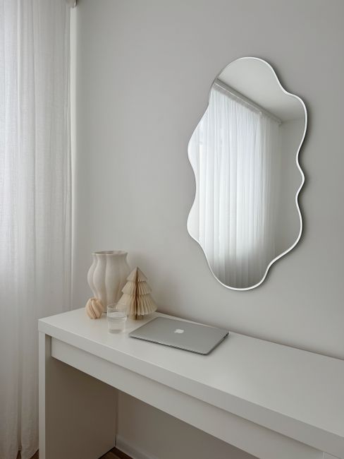 Stylish white minimalist workspace with abstract mirror and modern decor.
