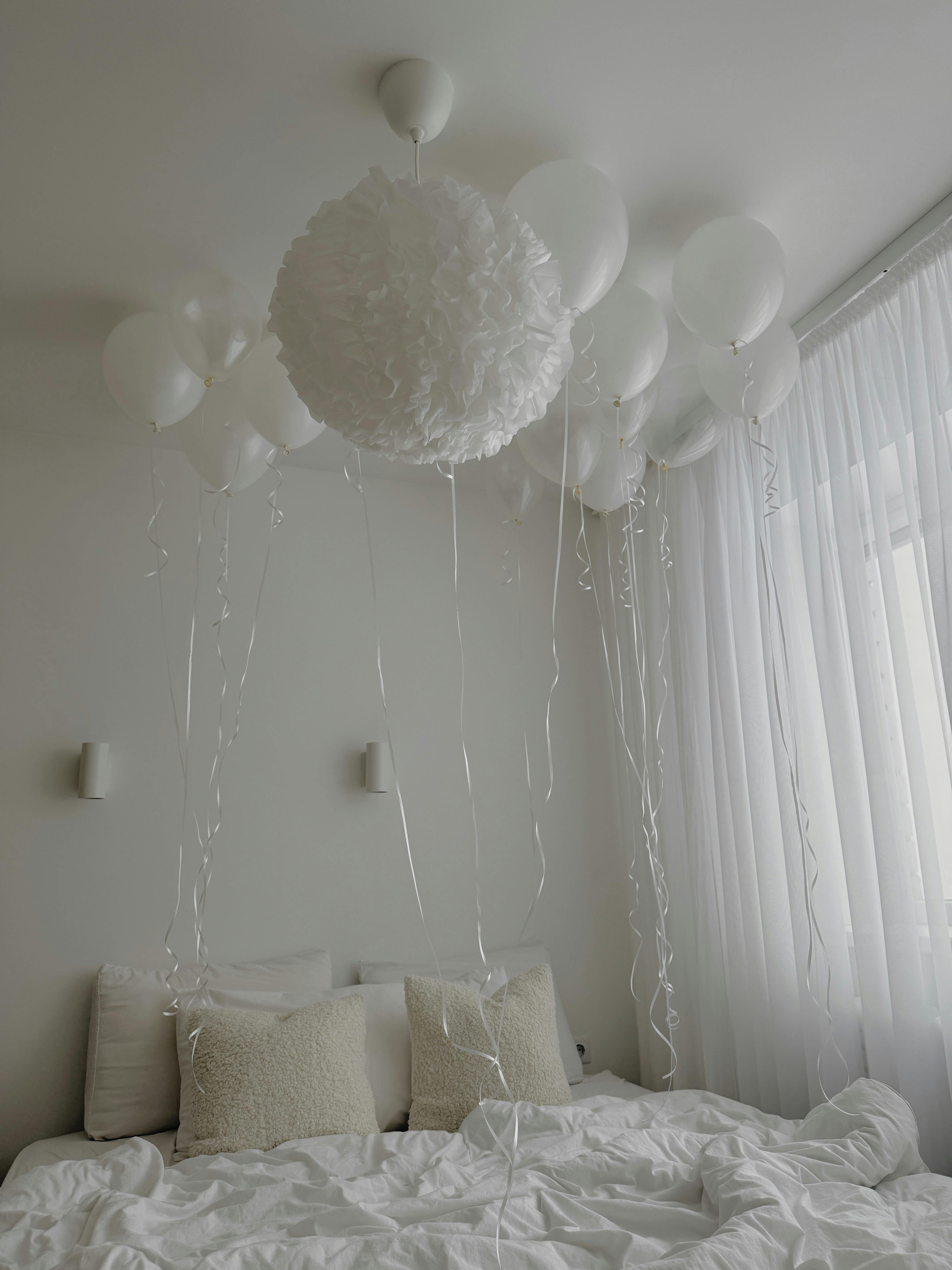 Serene white bedroom featuring elegant balloon decor and soft lighting for a calming atmosphere.