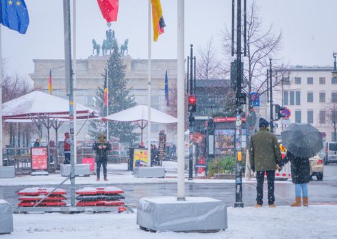 Snowy day at Brandenburg Gate, Berlin, with people and flags in view.