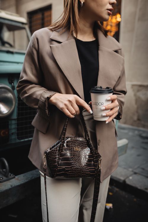 Free Stylish woman holding coffee cup and crocodile handbag in city setting, exuding modern fashion vibes. Stock Photo