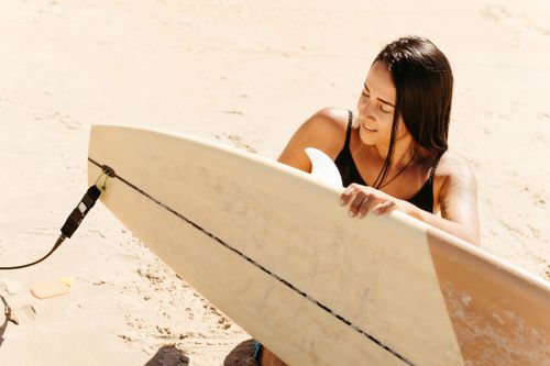 Free A woman enjoys a sunny day, holding a surfboard on a sandy beach. Stock Photo
