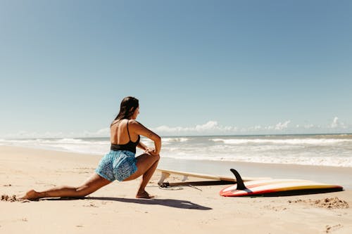 Young Woman Stretching before Surfing on the Beach 