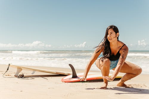 Woman Crouching on the Beach next to Surfboards 