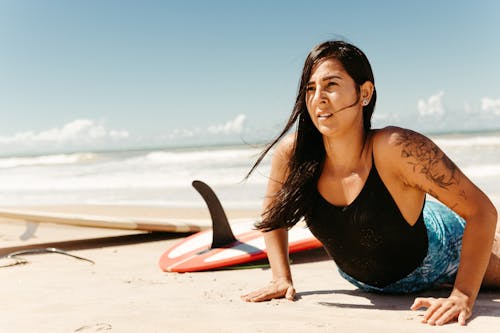 Woman Lying on Sandy Beach near Surfboards