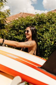 Smiling woman in sunglasses holding a surfboard, embracing the summer vibe outdoors.
