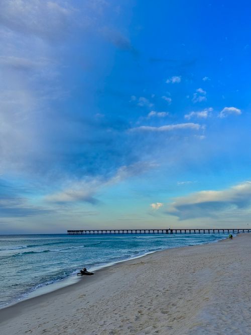 Free Serene beach scene featuring a long pier under expansive blue skies with gentle waves. Stock Photo
