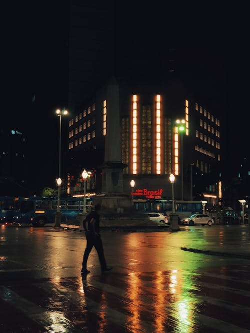 Illuminated Buildings and Man Crossing Wet Street