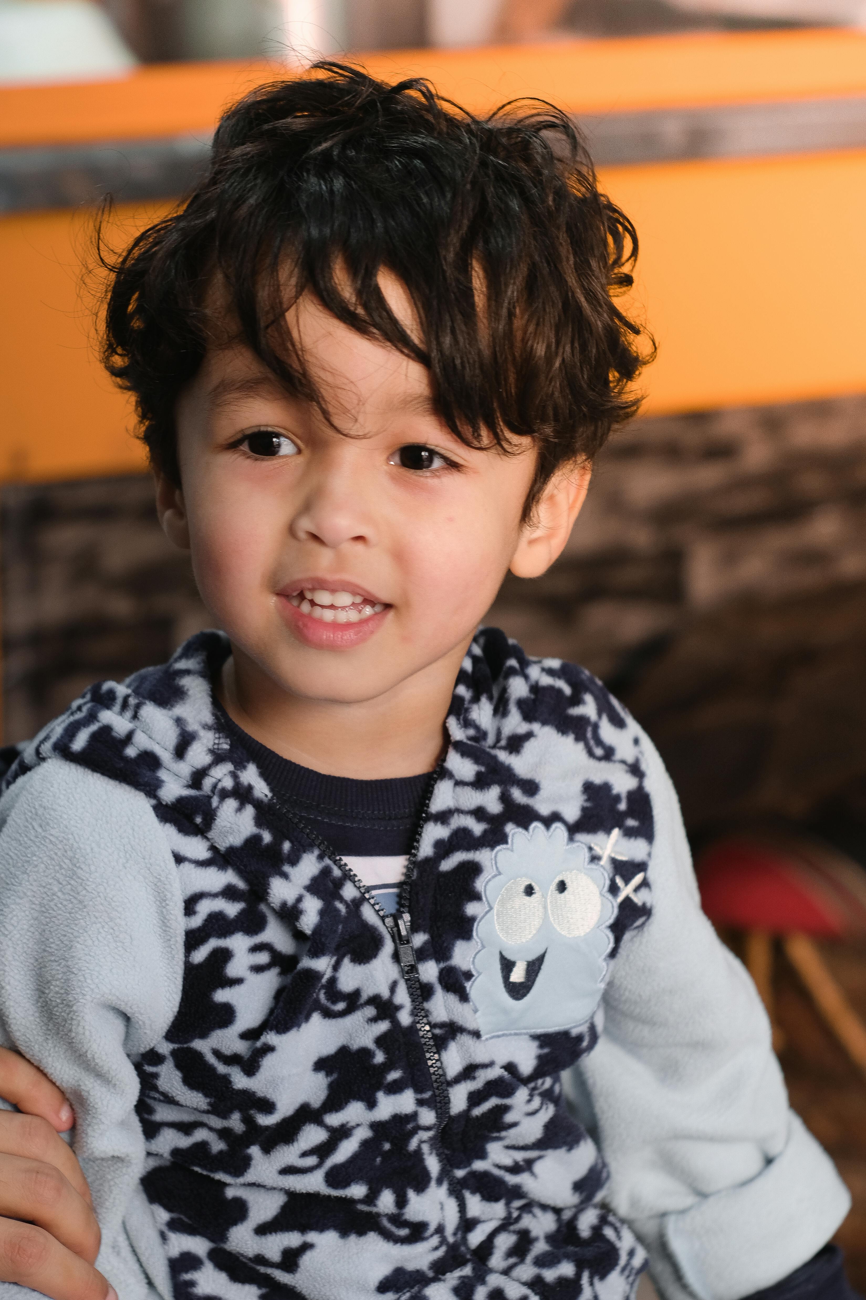 Cute child with curly hair smiling in casual clothes indoors.