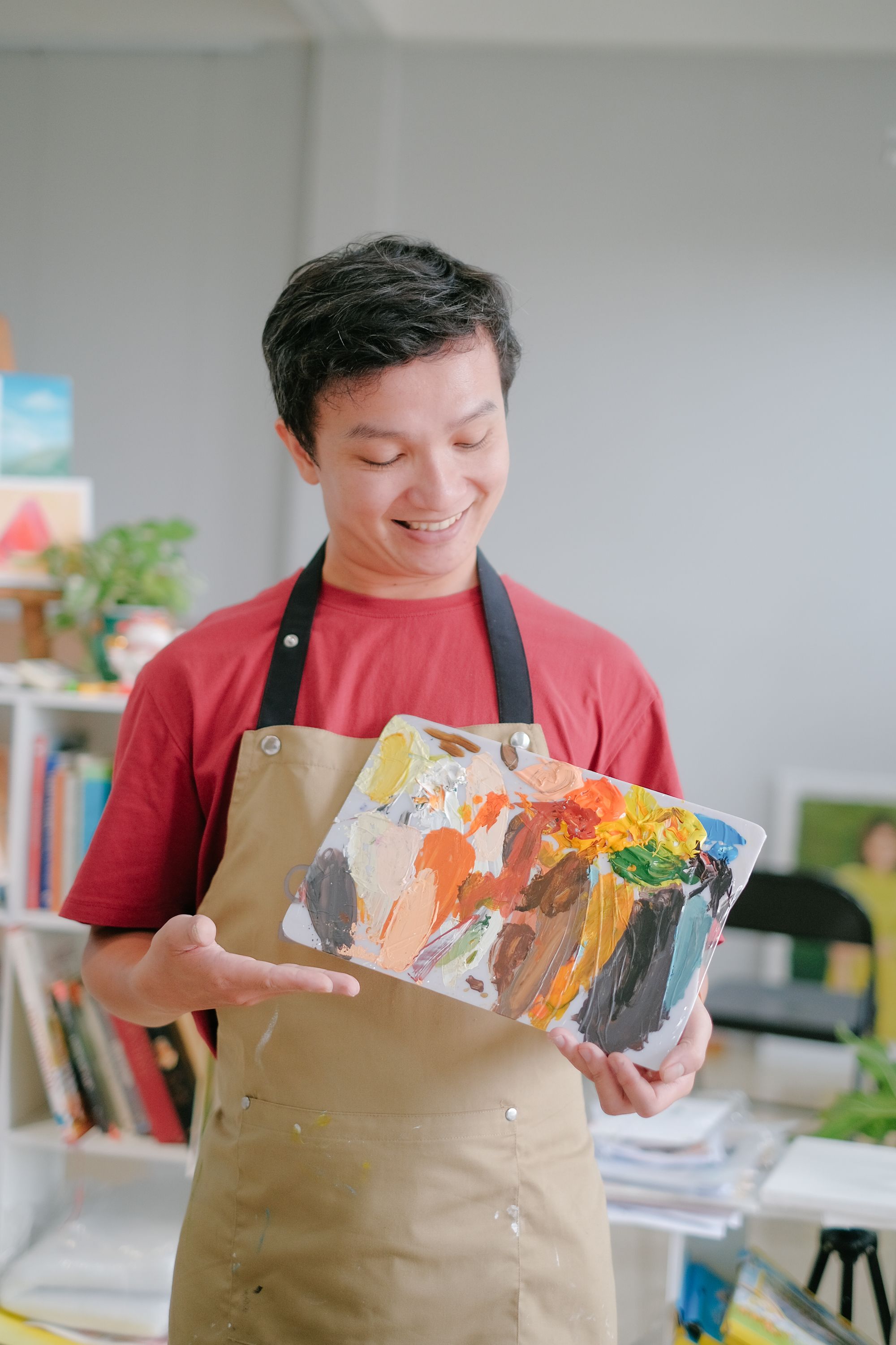 Young artist in apron showcasing a vibrant paint palette in a creative studio setting.
