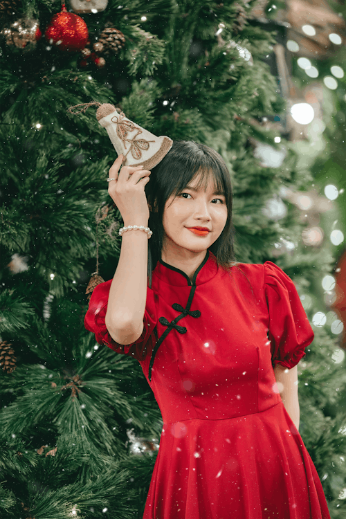Woman in Red Dress with Christmas Ball Standing by Christmas Tree