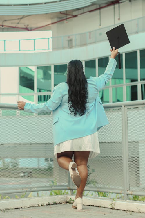 Back View of Graduate Holding Academic Hat in Raised Arm