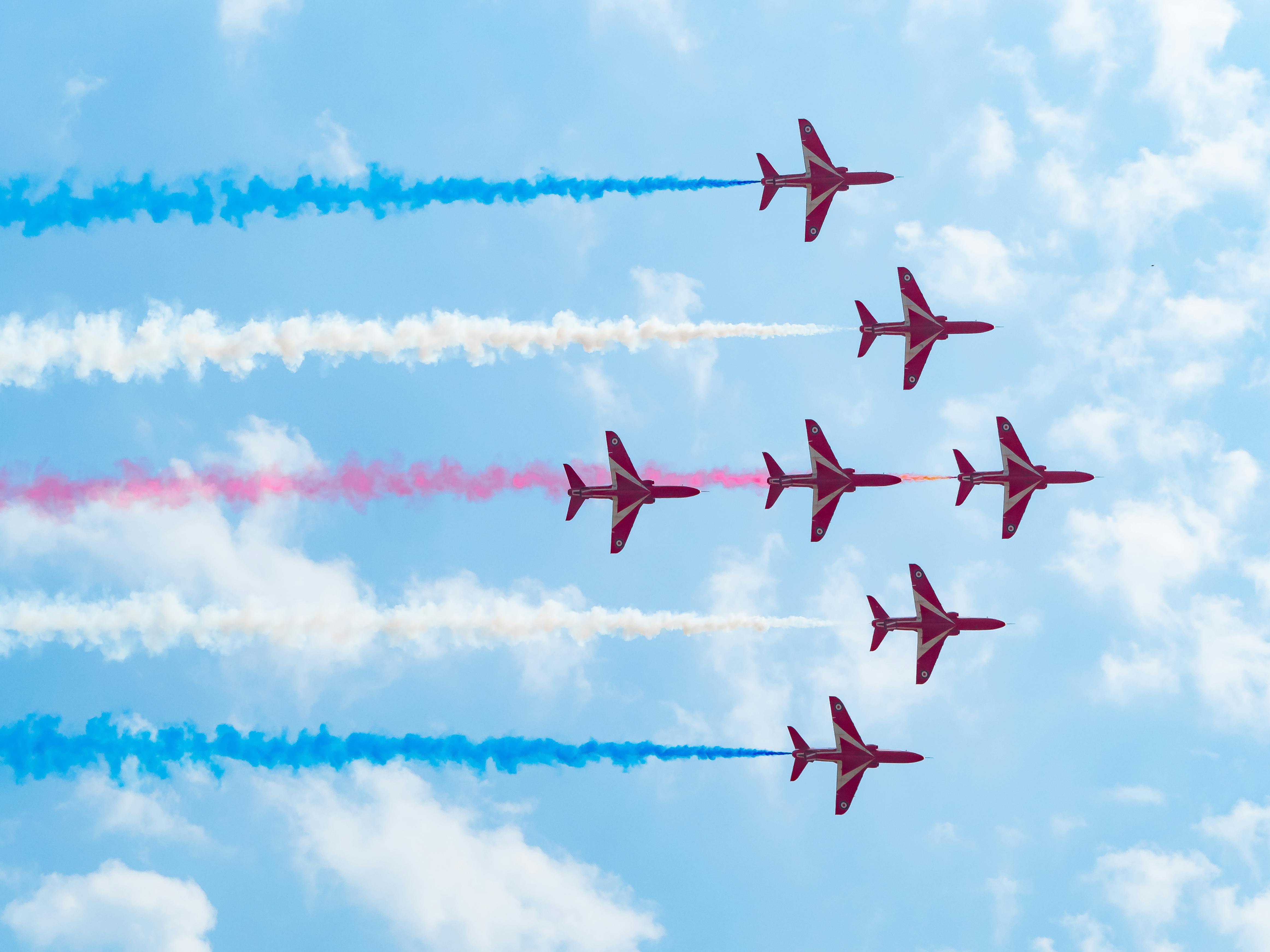 Red Arrows' aerobatic performance in Coningsby, UK, featuring colorful contrails against a clear sky.