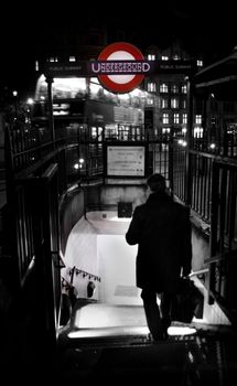 A dark, moody scene capturing a businessman entering a London Underground station at night.