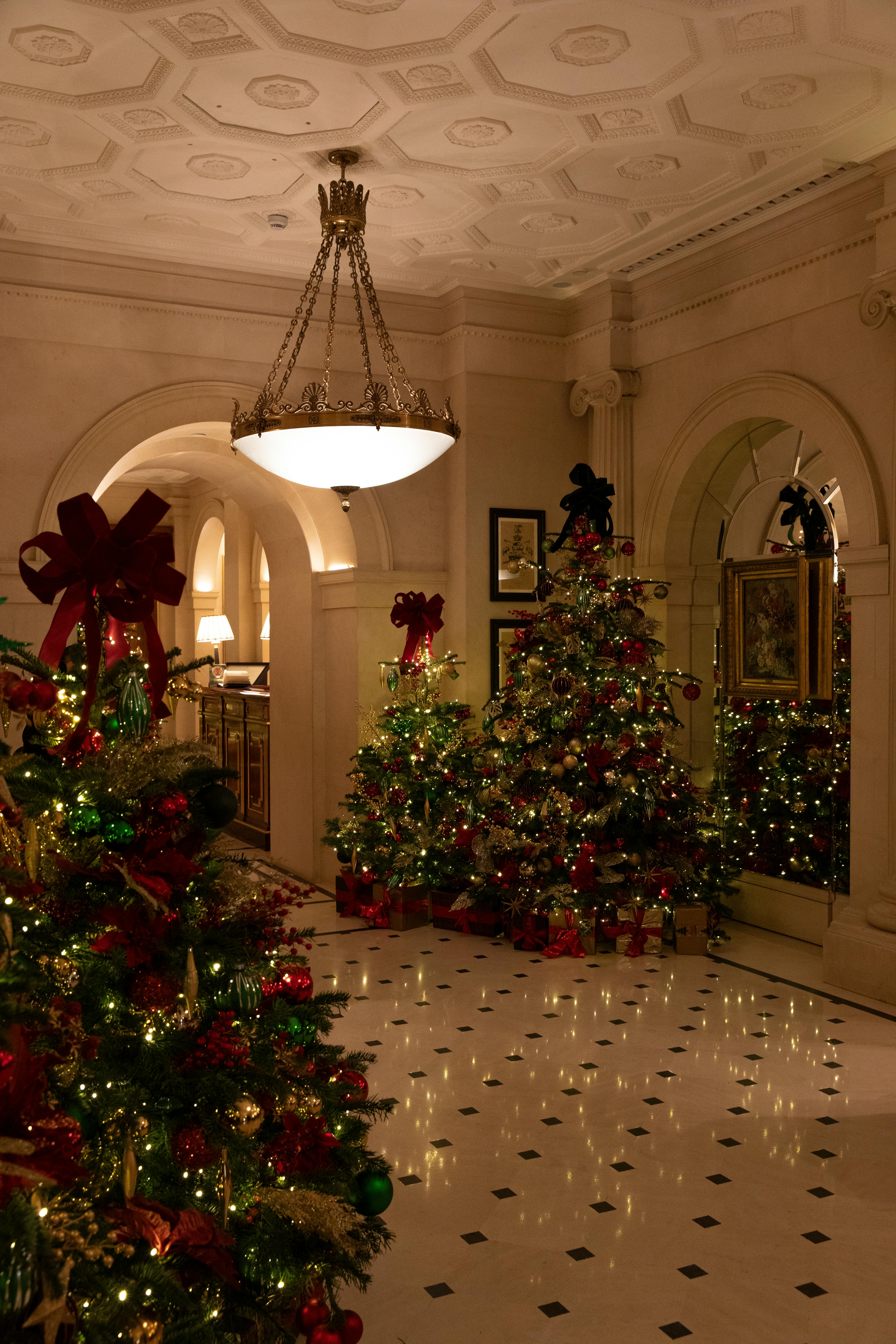 Elegant hotel lobby adorned with Christmas trees and chandelier in a festive setting.