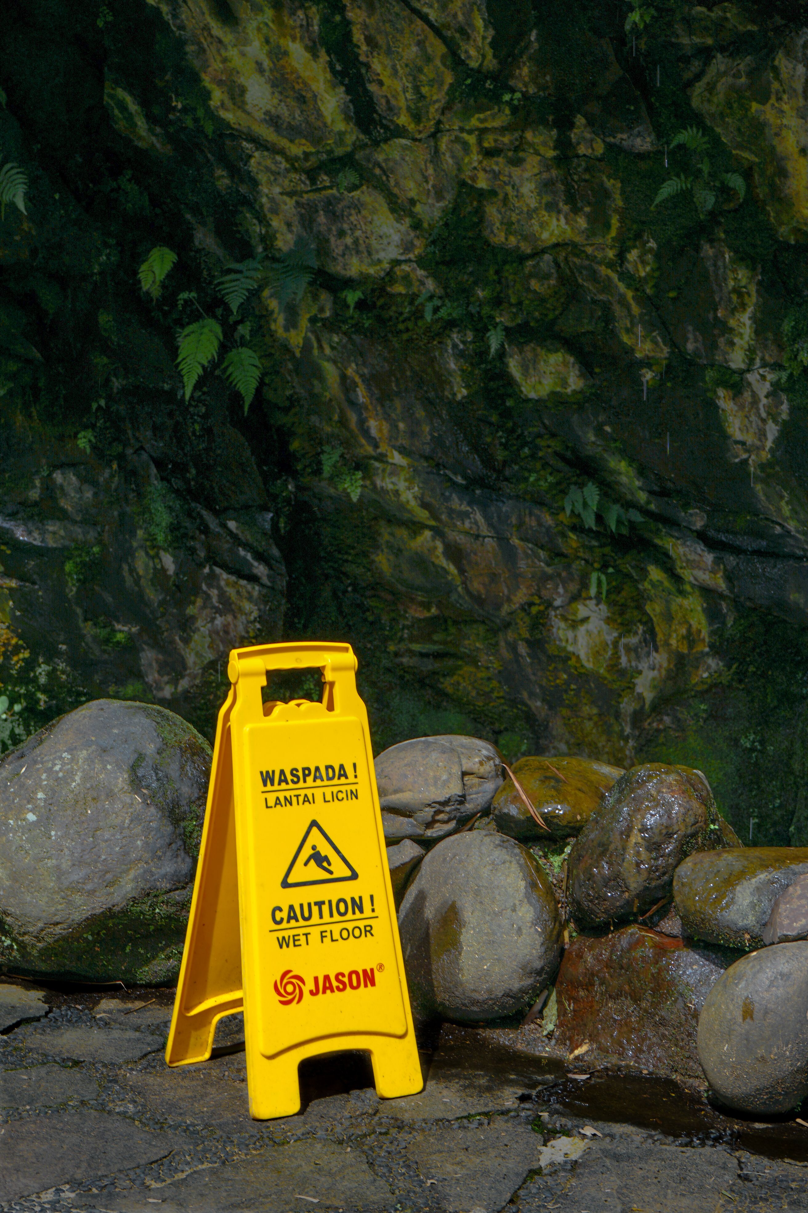 Yellow caution sign on wet rocks in Bandung, Indonesia warning of slippery floor.
