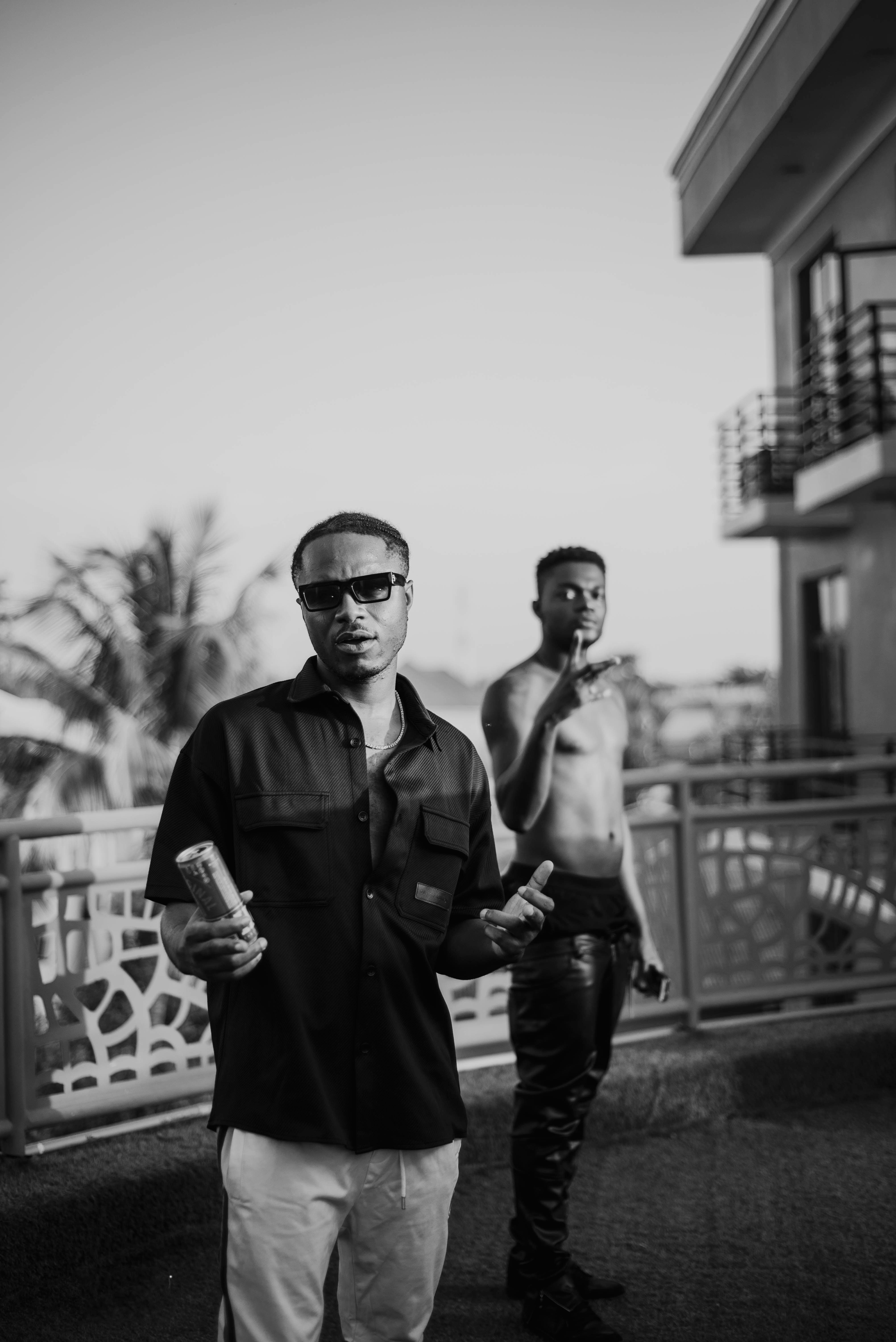 Black and white photo of two musicians on a terrace. One is shirtless.