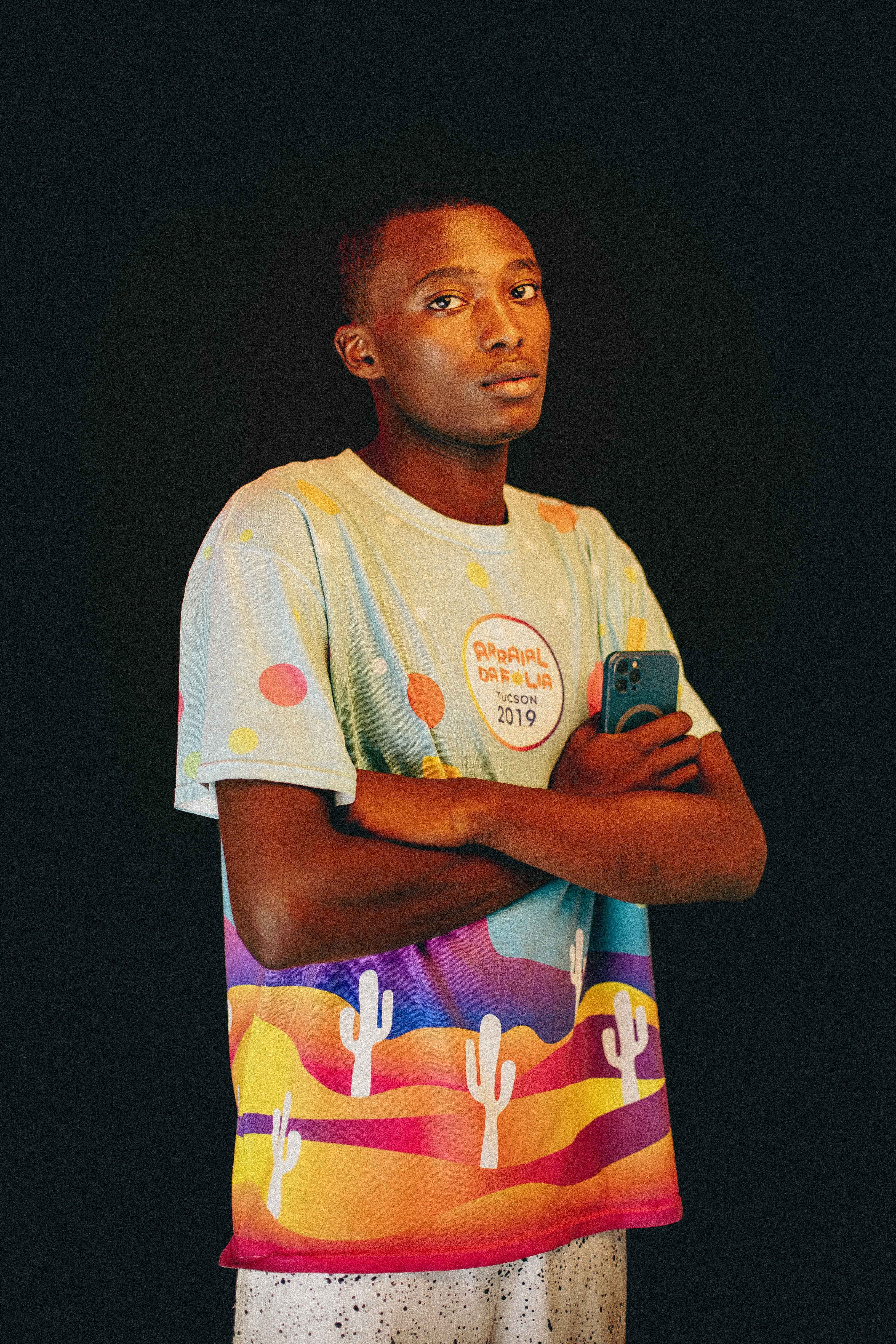Portrait of a man in a vibrant T-shirt holding a smartphone on a black background.