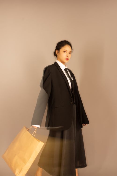 Free Fashionable Asian woman in elegant attire posing with a shopping bag in a studio setting. Stock Photo