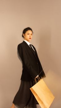 Stylish Asian woman posing with shopping bag in modern fashion, studio setting.