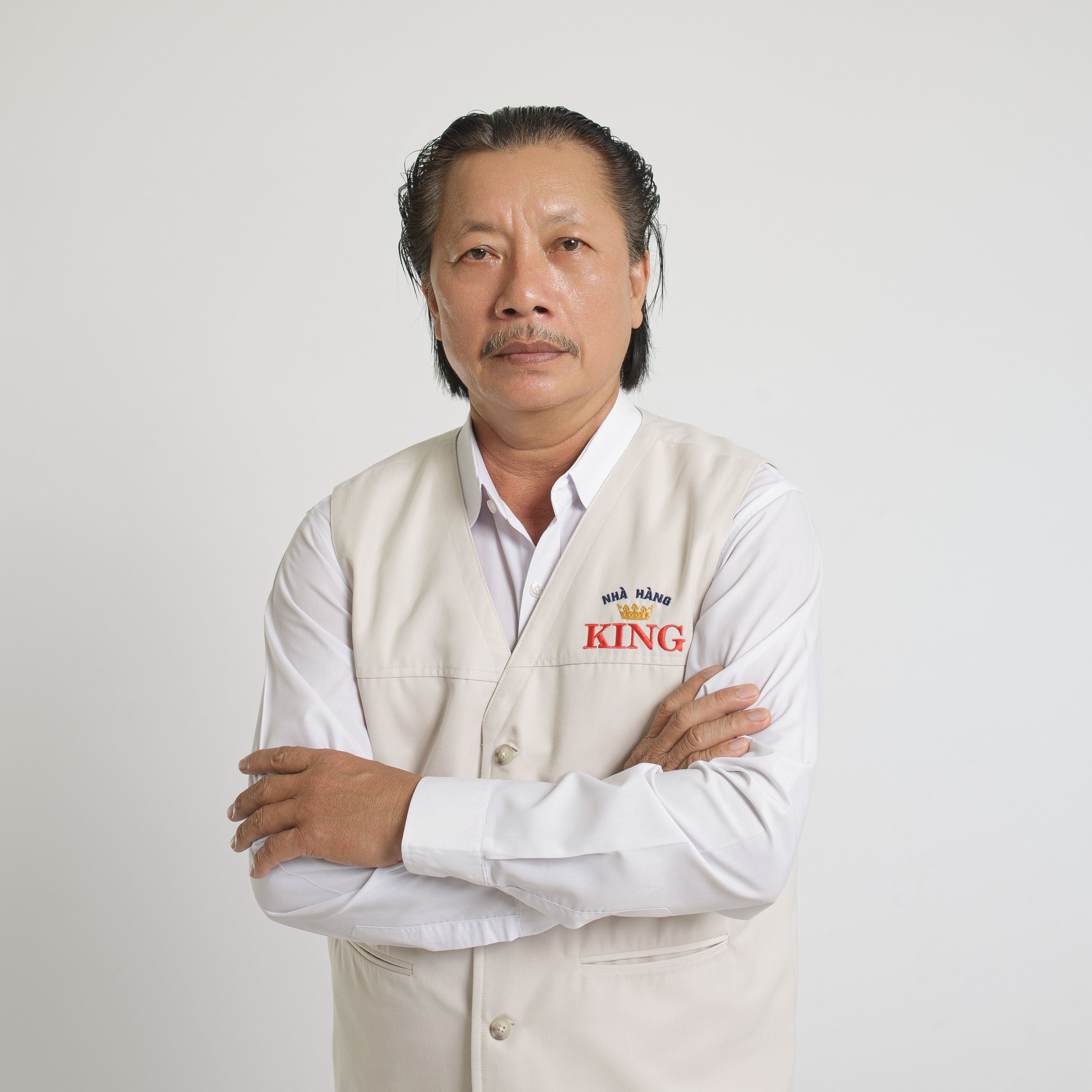 Elegant studio portrait of a mature man with arms crossed, wearing a white vest and shirt.