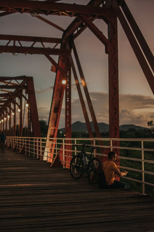 Man Sitting alone with a Bicycle on a Bridge 