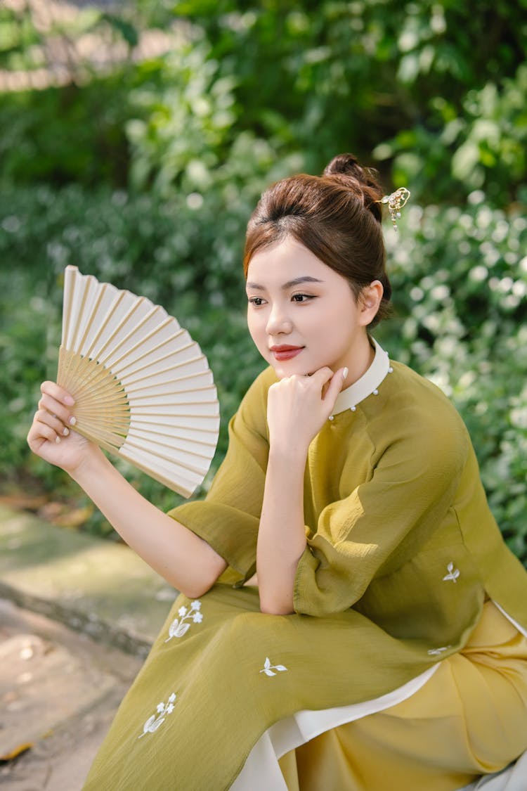 Young Woman Wearing An Ao Dai Dress And Holding A Fan 