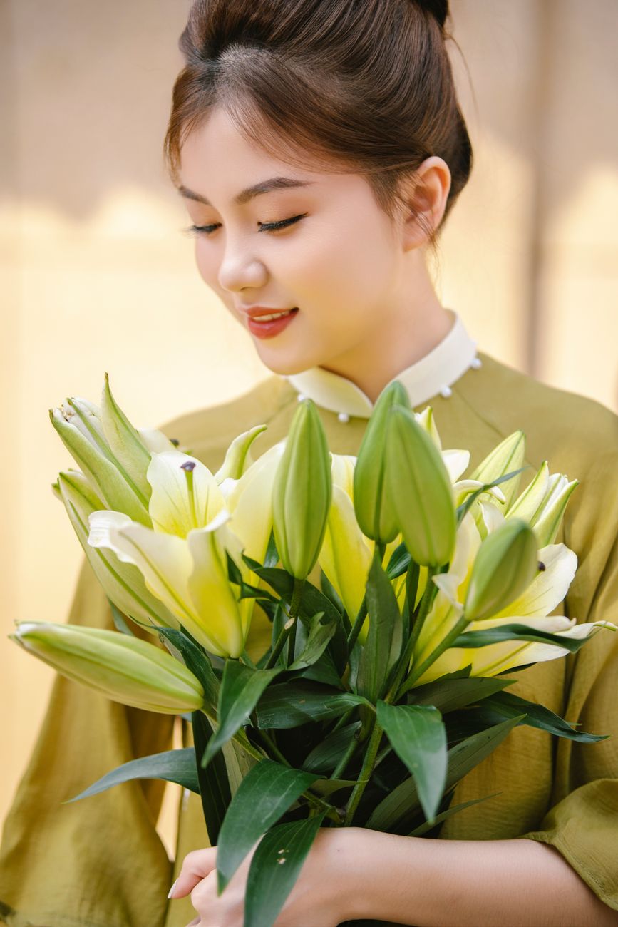Young woman in traditional Vietnamese Ao Dai holding a bouquet of lilies.