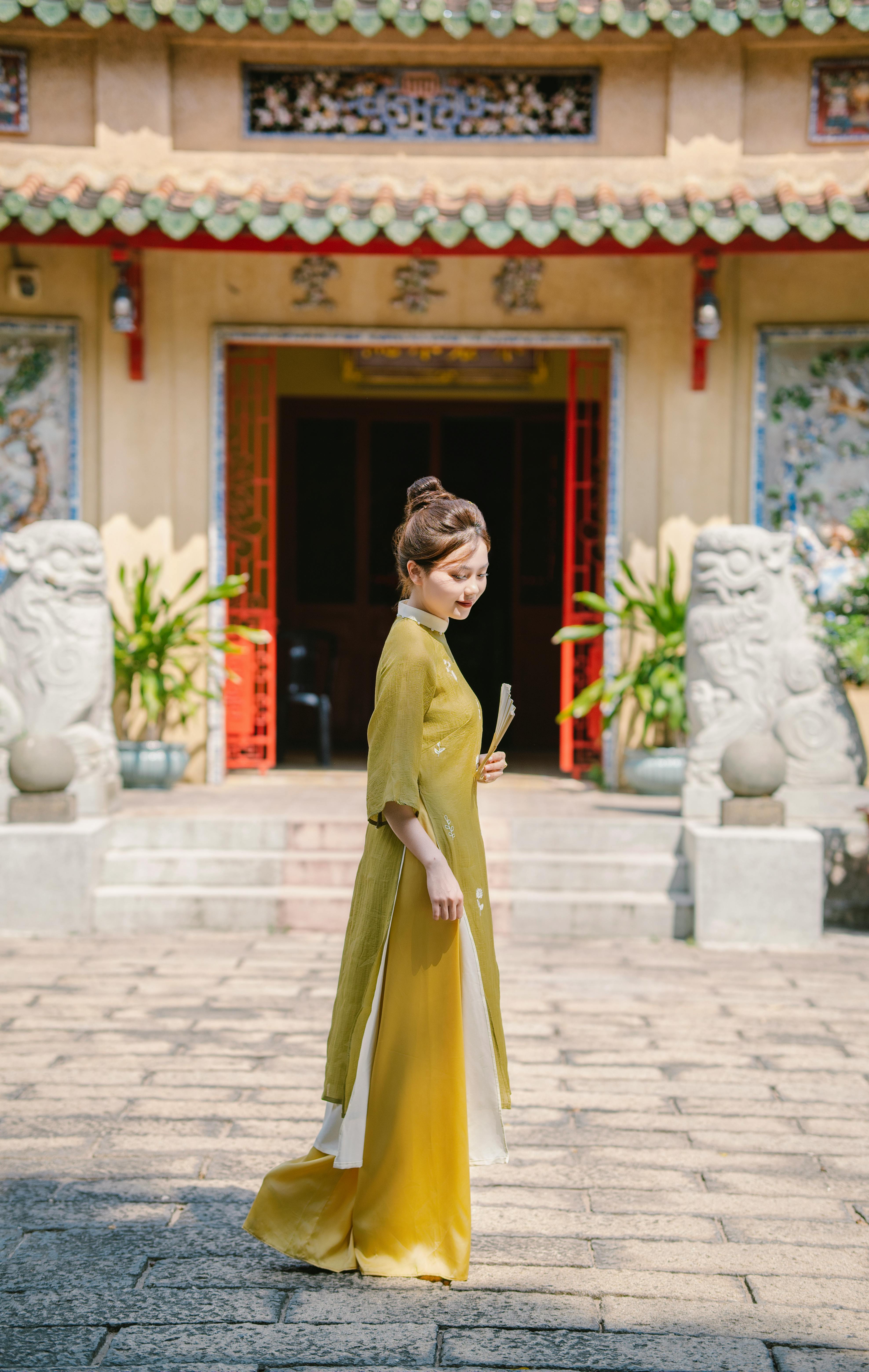 A woman in a yellow ao dai stands elegantly outside a Vietnamese temple.