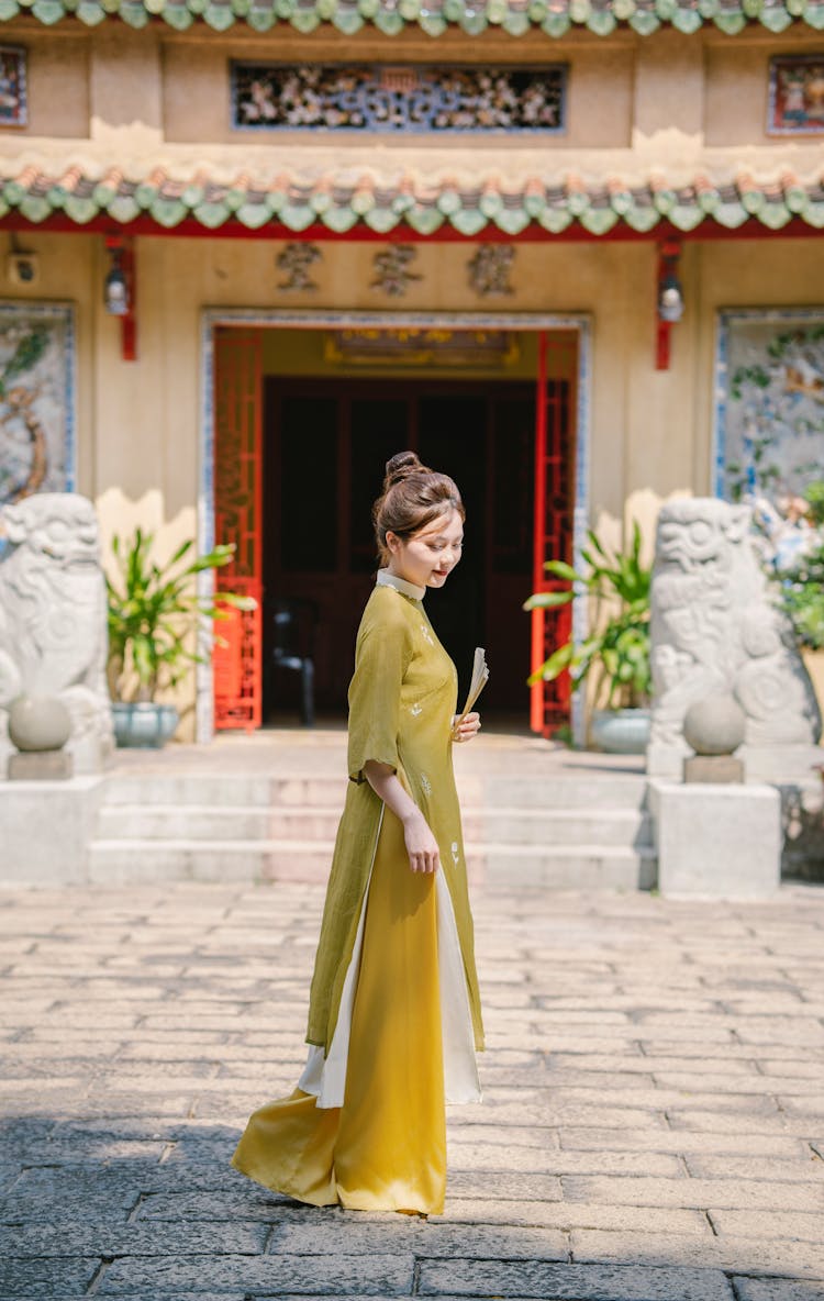 Young Woman In An Ao Dai Dress Standing In Front Of A Temple 