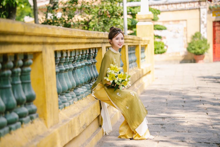 Young Woman In An Ao Dai Dress Holding A Bouquet Of Lilies