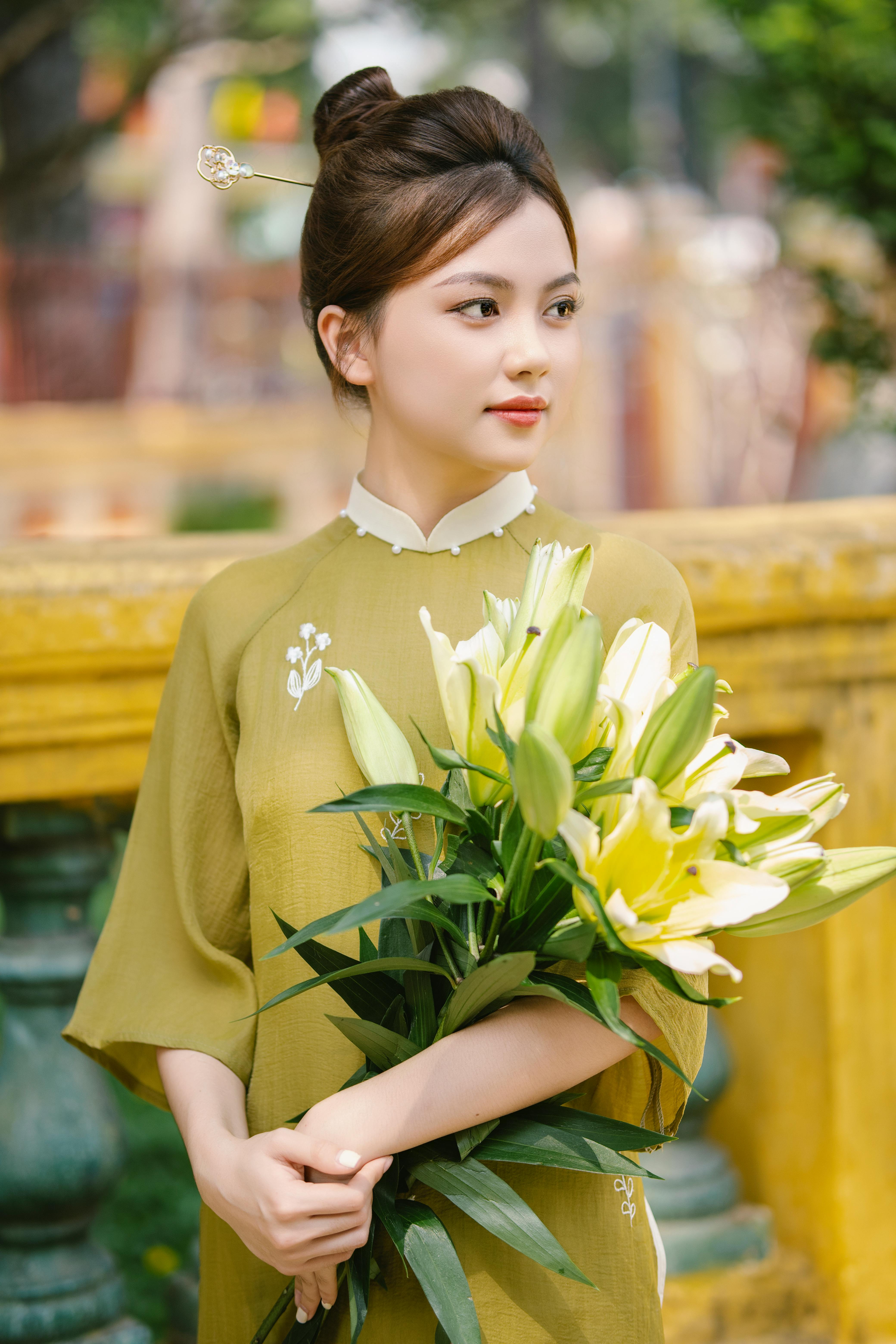 Young woman in traditional ao dai with bouquet of lilies, exuding grace and elegance.