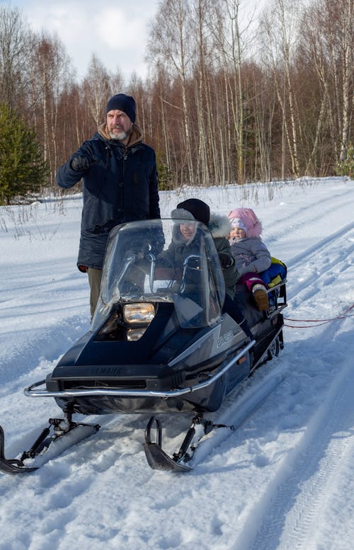 Father Standing by Kids Sitting on Snowmobile