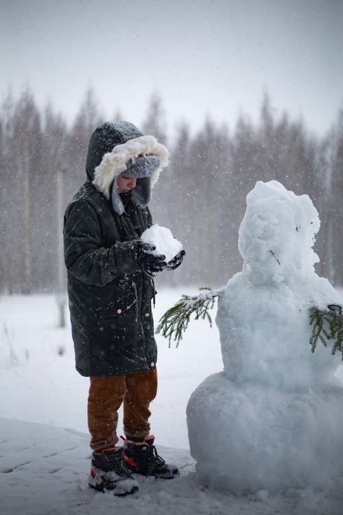 Free A child joyfully creates a snowman during a snowy winter day, capturing the essence of winter fun. Stock Photo