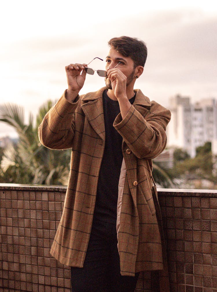 Young Man In A Checkered Coat Putting On Sunglasses 