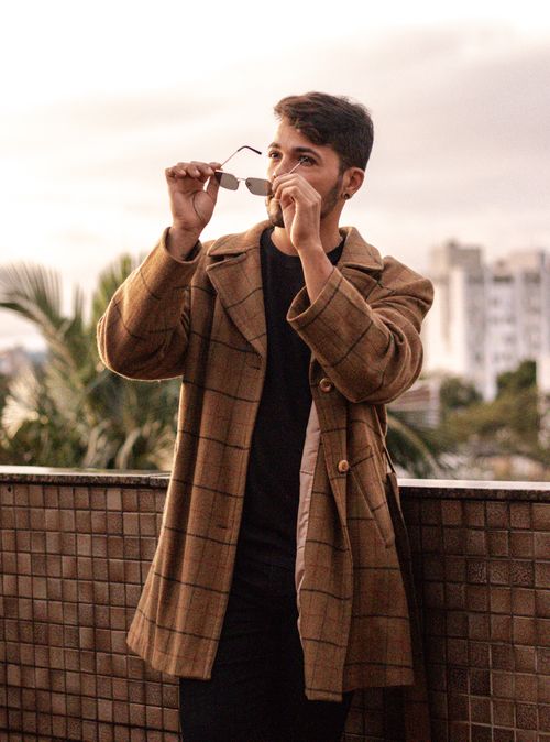 Free Man standing outdoors in checkered coat adjusting sunglasses, urban setting. Stock Photo