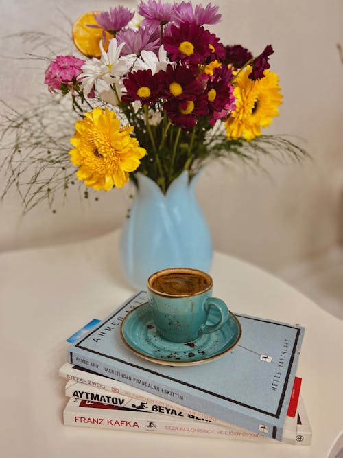 Free A Cup of Coffee Standing on a Pile of Books next to a Vase with Flowers Stock Photo