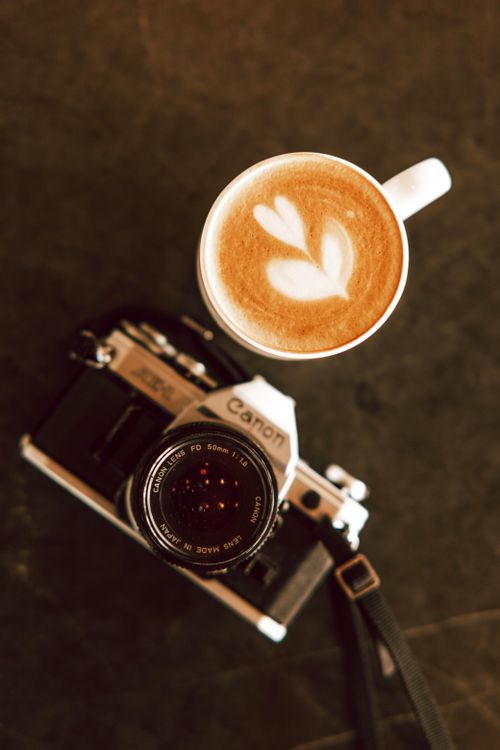 Free Top view of a latte with heart art next to a vintage camera on a dark surface. Stock Photo