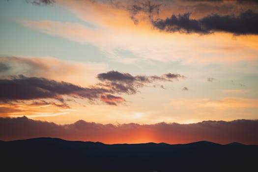 A breathtaking view of the sun setting behind mountains with vivid sky colors.