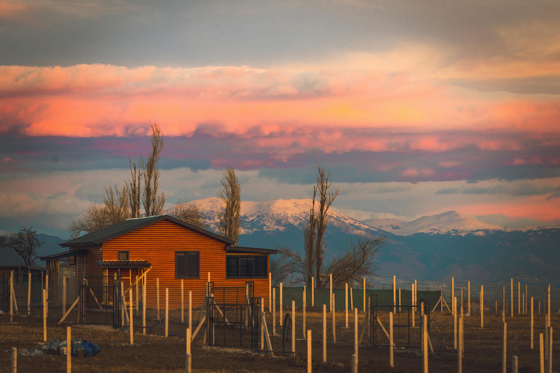 Cottage Among Fenced Plots in a Valley with Snowcapped Mountains in the Background