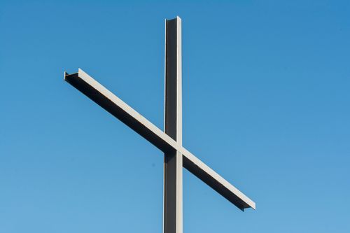 Free A metal cross stands silhouetted against a vivid blue sky, symbolizing faith and spirituality. Stock Photo