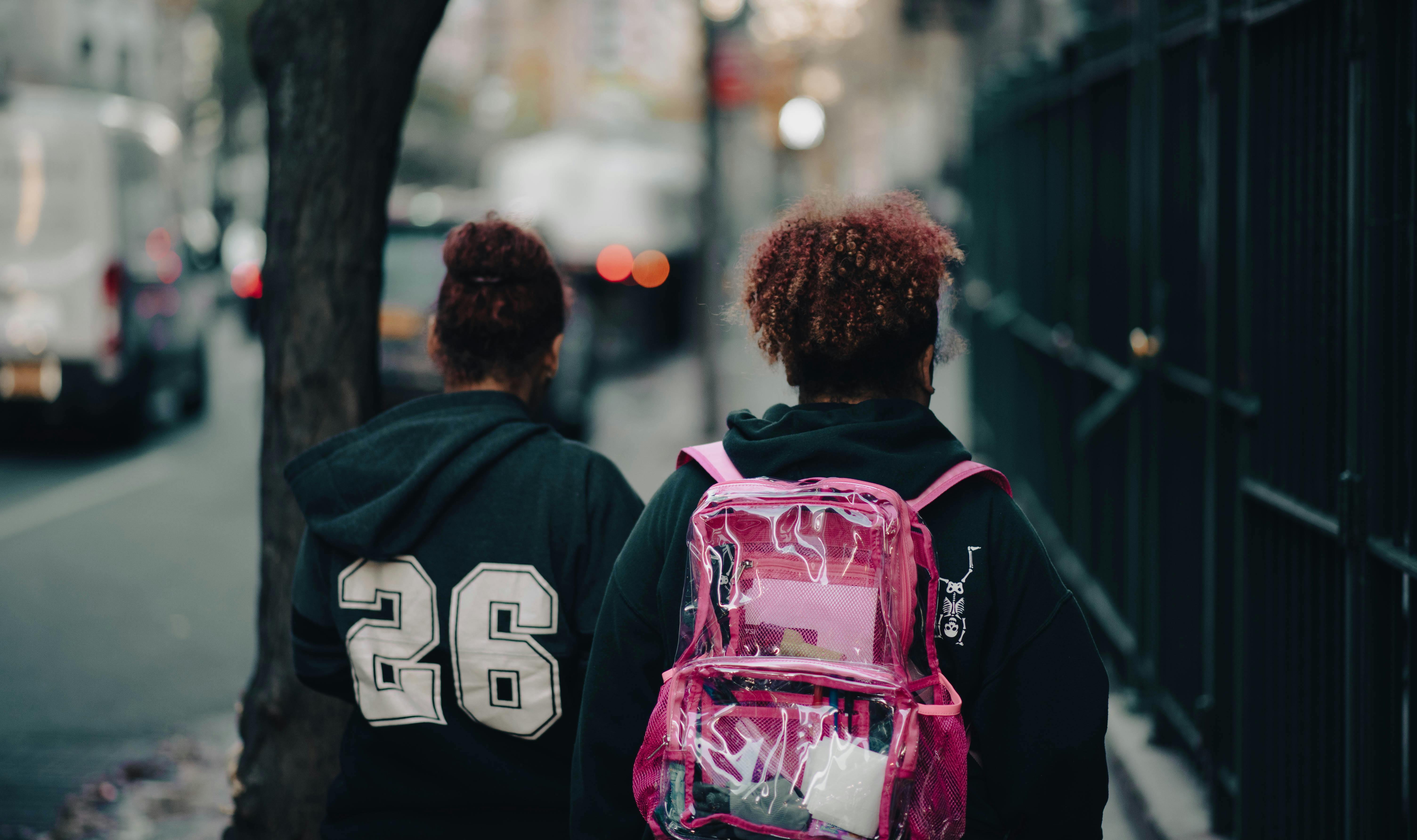Two students walk through an urban street in New York City, with backpacks and casual attire.