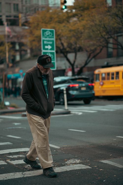 Free Elderly man with hands in pockets walking on NYC crosswalk with a yellow school bus in the background. Stock Photo