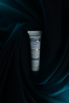 Whitening cream tube on luxurious dark green fabric, perfect for skincare ads.