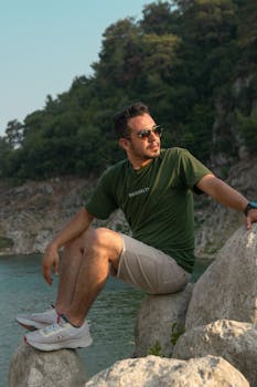 Man sitting on rocks by the sea, wearing casual attire, enjoying the summer day.