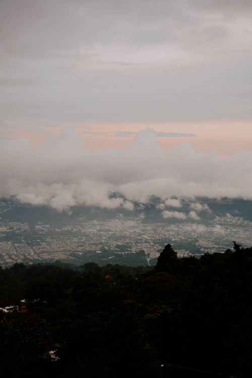 Free Breathtaking view of a city partially covered by clouds, captured at dawn with a scenic mountainous backdrop. Stock Photo