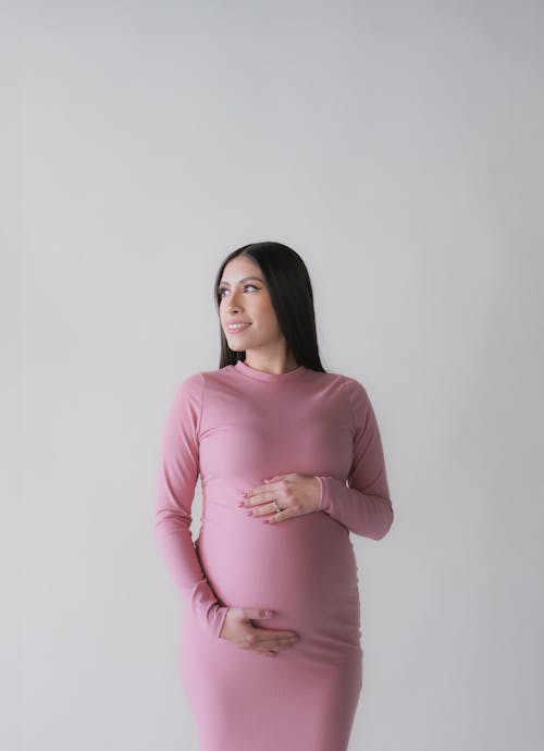 Pregnant Woman in a Pink Dress Touching Her Stomach and Smiling 
