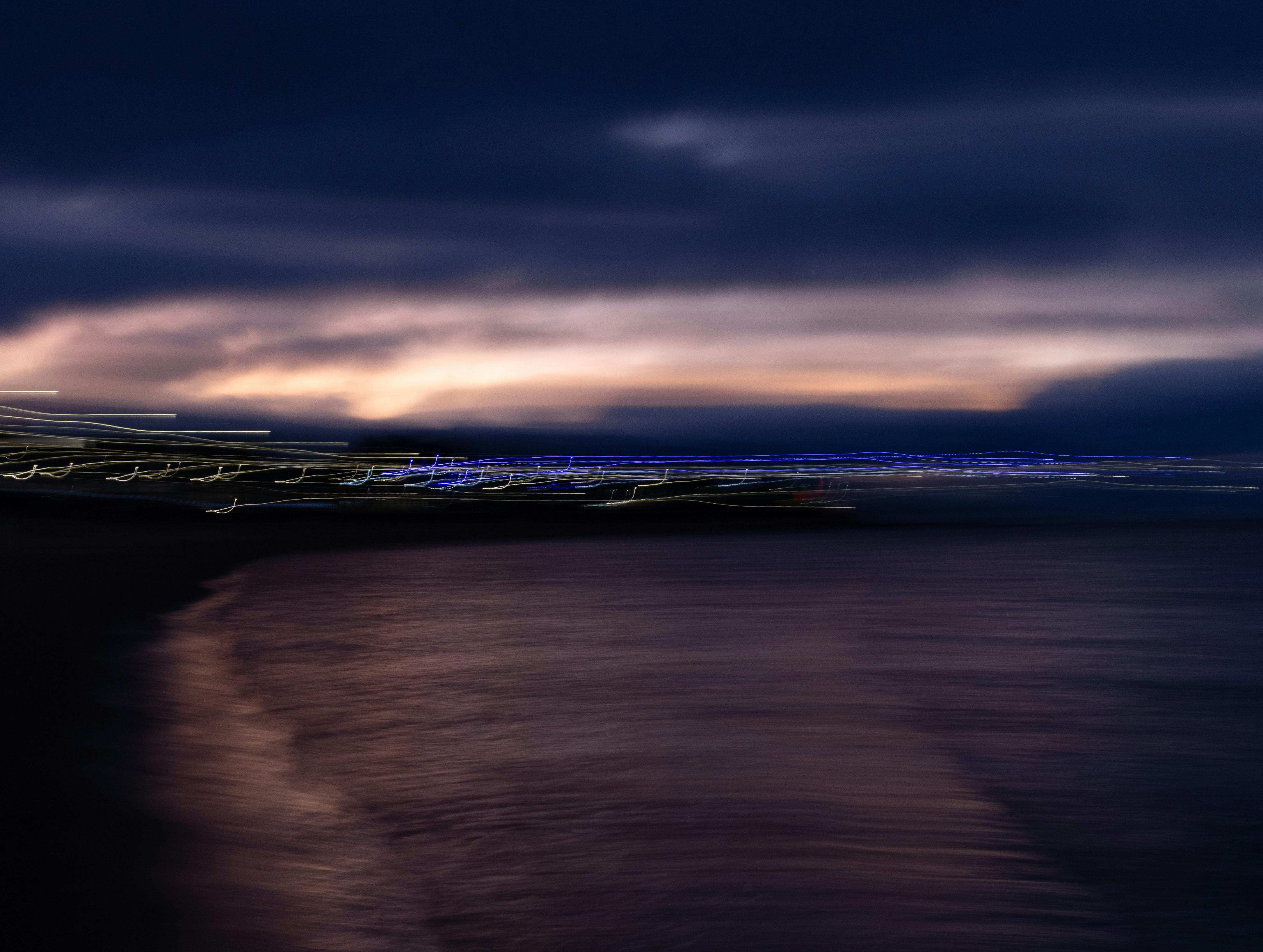 An abstract coastal image at dusk displaying blurred light effects over water and sky.